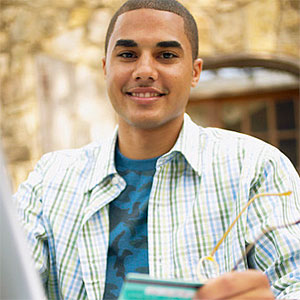Young man sitting at a table in front of a laptop holding a credit card © Jack Hollingsworth, Blend Images, Getty Images