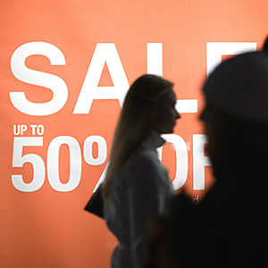 Poster proclaiming Sale up to 50% off and shoppers silhouetted in foreground © Michele Constantini/PhotoAlto Agency RF/Getty Images