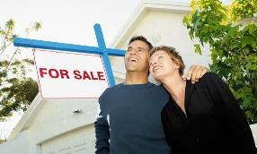 Couple stand next to a for-sale sign. © Corbis