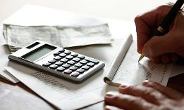 Man writing check, calculator, bills (© Dana Hoff/Getty Images)