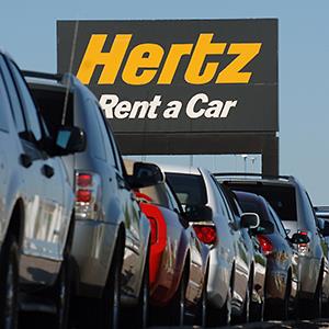 Credit: © Matthew Staver/Bloomberg via Getty Images
Caption: A row of rental cars are parked below a sign for Hertz Corp. at Denver International Airport